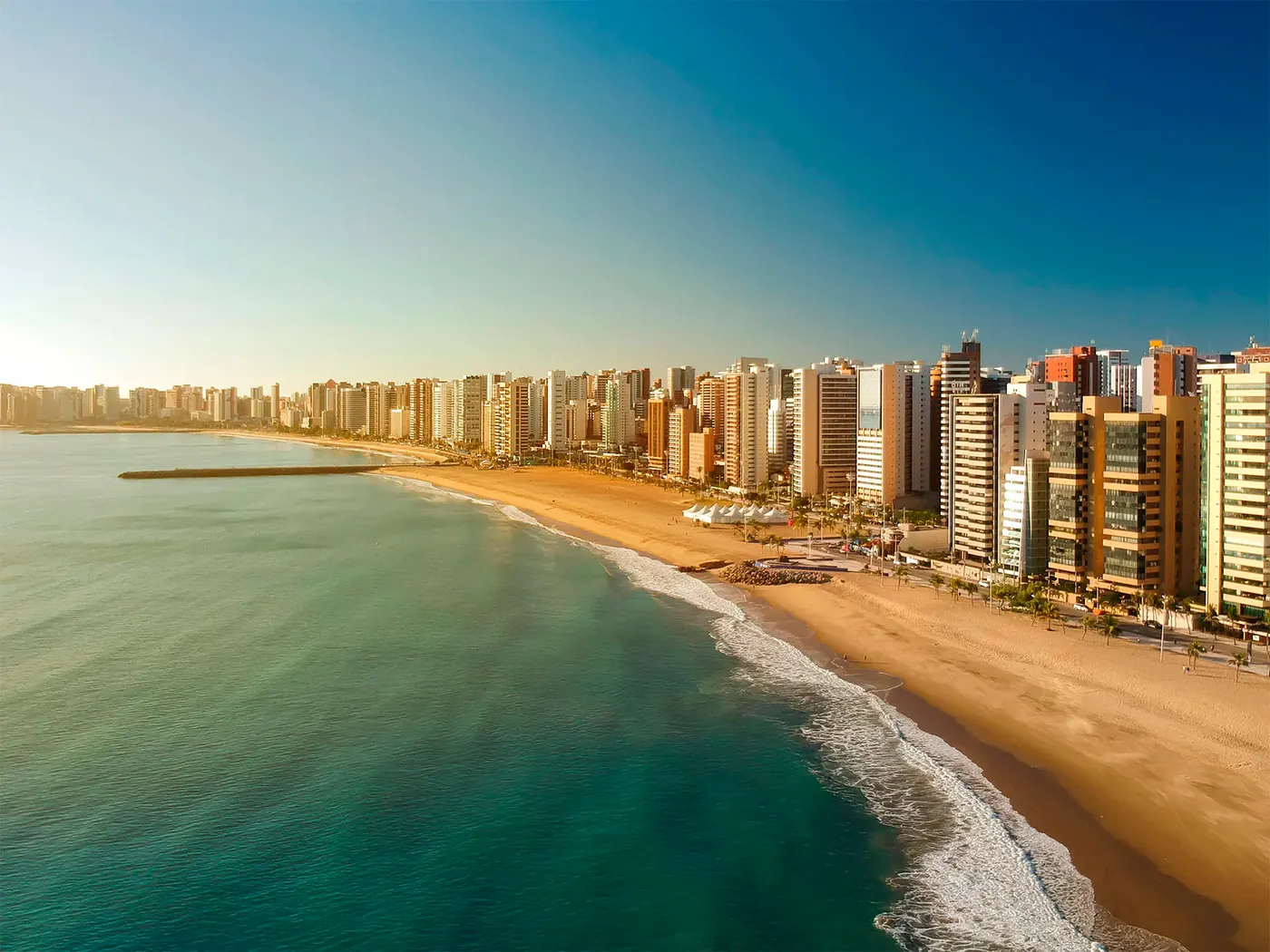 Vista aérea do litoral cearense, com a praia e a cidade ao fundo.